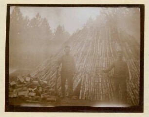 Foto zweier Soldaten vor dem fertig gestapelten Holz für einen Meiler in der Köhlerei bei der Köhlerwiese
