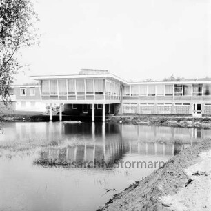 Am Exerzierplatz: Sportlerheim, links davon das Hausmeisterwohnheim, im Hintergrund das Rathausgebäude, vorne ein Teich: Blick von Südwesten