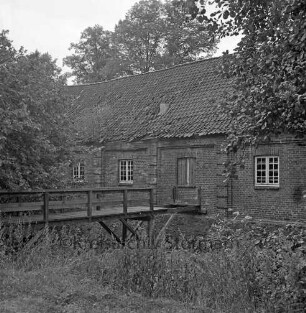 Denkmal: Kupfermühle mit beschädigtem Dach und in desolatem Zustand: vorn links beschädigte Holzbrücke über Glinder Au: davor Sträucher: hinten Bäume
