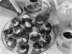 Krafts Rezeptaufnahmen. Glasteller mit gefüllten Windbeuteln. Daneben Serviettenständer, Kaffeetassen, Sahnekännchen und Kaffeekanne