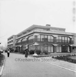 Seniorenwohnanlage Rosenhof I: Hoisdorfer Landstraße: Außenansicht des Gebäudekomplexes: vorn Zuwegung: darauf links zwei Frauen und hinten Pkw: rechts und links Grünanlage
