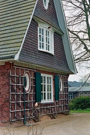 An den Stücken (7): Wohnhaus aus Backstein: Giebelseite, ovale Fenster, Sprossenfenster mit Fensterläden, Rankgerüst, an Giebel Schindelverkleidung, vorgewölbtes Sprossenfenster