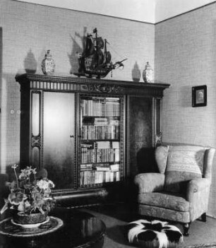 Holleischen (Holýšov). Wohnhaus. Wohnzimmer. Sessel neben einem Bücherschrank mit Schiffsmodell