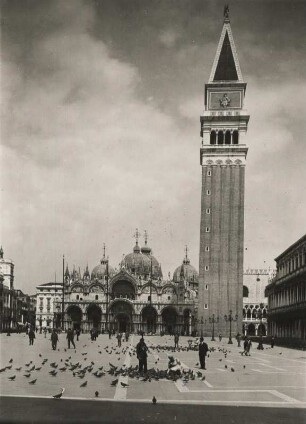 Venedig. Italien. Markusplatz mit Blick auf die, im byzantinischen Stil errichtetee Basilica di San Marco (Markusdom) und den Campanile di San Marco (Glockenturm). Passanten füttern Tauben