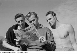 Portrait Hans Haberhauffes, Paul Tiedemanns und eines weiteren Mannes bei der Lektüre der Zeitung "Der Handball" auf dem Sportplatz der Sportschule