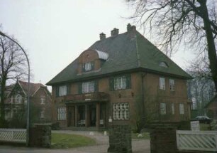 Kirchstraße 10: traufständiges Backsteinhaus mit Walmdach: Straßenfront mit Pfeilerportikus, Eingangstür, Altan, Gaube mit Bogendach: davor Auffahrt