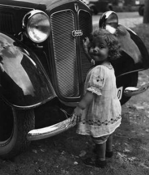 Kinderbilder. Kleines Mädchen vor der Kühlerhaube eines Autos (vielleicht in Ellingen)