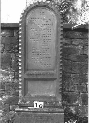 Grabstein 16 (Index: 100114422) Material: Sandstein Zustand: Sockel leicht verwittert Maße HxBxT: 154x57x27 cm Beschreibung: Stele, getreppter Sockel, Rundbogenabschluß Symbolik: umlaufendes Bogenfries: Grabstein 16