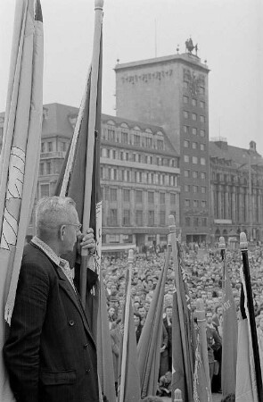 Portrait eines Mannes mit einer Fahne in der Hand auf dem Podium bei einer Demonstration auf dem Karl-Marx-Platz