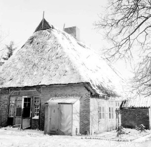 Reetdachkate mit mehreren kleinen Anbauten: rechts davor Baum: Gebäude der ehemaligen Dorfschule von 1835: Winter