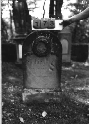 Grabstein 173 (Index: 100110642) Material: Sandstein Zustand: leicht verwittert, geringer Textverlust Maße HxBxT: 99x55x16 cm Beschreibung: Stele, Sockel, Rundbogenabschluß Symbolik: Kranz mit Band: Grabstein 173