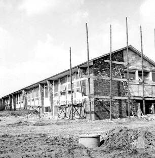 Volksschule: Erweiterungsbau: Rohbau: rechts an Giebelwand Gerüste und Leiter: vorn Erdhaufen und Kanalisationsrohr