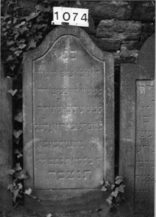 Grabstein 1074 (Index: 99630577) Material: Sandstein Zustand: stark verwittert Maße HxBxT: 120x58x7 cm Beschreibung: Stele mit Konvexbogenabschluß, Schriftfeld eingetieft: Grabstein 1074