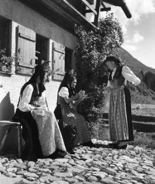 Drei Frauen in Trachten vor einem Bauernhaus. Zwei beim Wolle Wickeln (vielleicht im Walsertal)