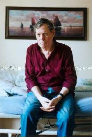 Älterer, männlicher Heimbewohner auf dem Bett sitzend (Prämiertes Foto)