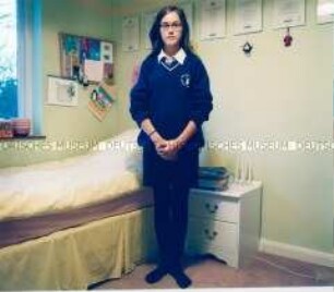 Mädchen in Schuluniform vor einem Bett (Altersgruppe 18-21)