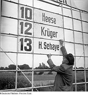 Rennplatzangestellter bestückt Anzeigetafel mit Startnummern und Namensschildern von Jockeis