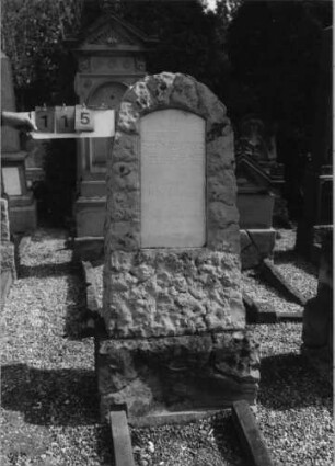Grabstein 115 (Index: 99796763) Material: Kalkst. ?, Sock-Sandstein, weiße Marmorplat Zustand: gut Maße HxBxT: 158x57x37 cm Beschreibung: konische Stele, rustica, Sockel, rustica, Segmentbogenabschluß, Schriftplatte: Grabstein 115