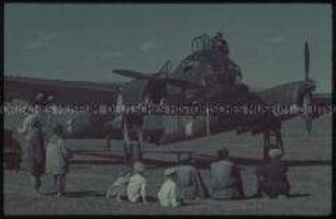 Einheimische vor einem Flugzeug der deutschen Wehrmacht sitzend