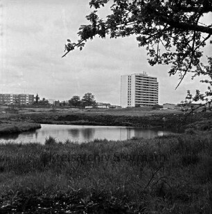 Neubaugebiet Ehmkenberg: vorn Teich und Wiese: dahinter unbebautes Gelände mit Erdhaufen, Bauwagen und Hütte: dahinter rechts Hochhaus am Poggenseer Weg: links Wohnblocks, in der Mitte Flachbauten