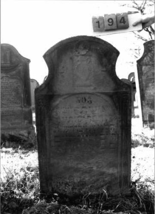 Grabstein 194 (Index: 100116358) Material: Sandstein Zustand: verwittert Maße HxBxT: 123x68x16 cm Beschreibung: Stele mit konkav eingezogenem Segmentbogenabschluß, eingetieftes Schriftfeld mit Rundbogenabschluß Symbolik: Levitenkanne, Blüte, Ranken: Grabstein 194