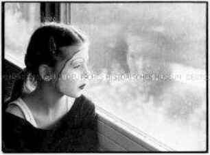 Mädchen mit geschminktem Gesicht schaut zum Fenster heraus (Altersgruppe 18-21)
