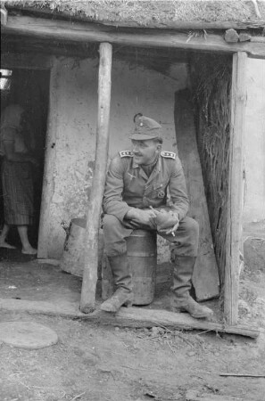 Zweiter Weltkrieg. Zur Einquartierung. Sowjetunion. Angehöriger der deutschen Wehrmacht, vor einer Bauernhütte sitzend
