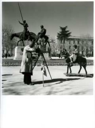 Mädchen posiert auf einem Spielpferd vor den Statuen der Protagonisten aus Don Quichote auf der Plaza de España in Madrid