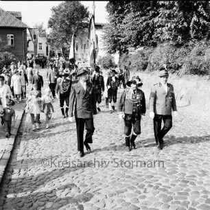 Schützenfest: Veranstalter Schützenverein Reinfeld und Umgebung von 1954 e.V.: Umzug: Paul-von-Schoenaich-Straße: Tiroler Schützen der Schützenkompanie Wilten (bei Innsbruck) mit Fahne, voran Hauptmann Karl Sagstetter: dahinter Schützenvereine mit Fahnen, Feuerwehrkapelle: links Zuschauer, Fahnenschmuck: rechts Böschung zum Kirchsteig: Bildmitte hinten Hotel Stadt Hamburg, Ahrensböker Straße, 8. September 1963