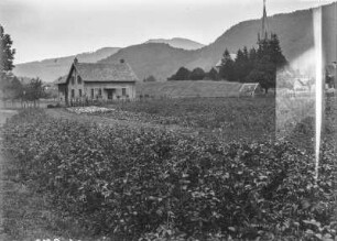 Dorf : Blick auf ein Dorf in einer Hochebene. Rechts eine Kirche, im Vordergrund Felder, im Hintergrund bewaldete Berghänge