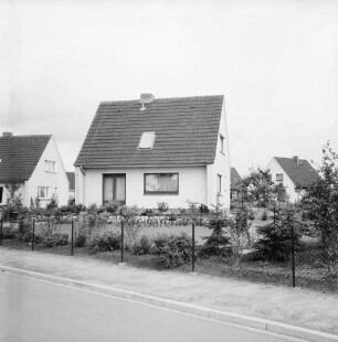 Am Saalteich: Neubausiedlung: vorn Zaun: dahinter Garten mit Bäumen und Sträuchern: dahinter Einfamilienhäuser