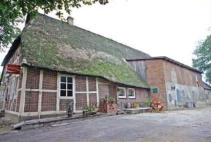 Papierholz 1: Fachwerkhaus mit Reetdach: Gasthaus Zur Hahnheide: nördliche Traufseite mit Wohnungstür, rechts Wirtschaftstrakt: links Giebelfront mit Eingangtür, Namensschild, Laternen, Reklameschilder