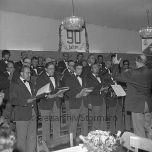 Männergesangverein "Liedertafel Siek von 1886" e.V.: 90-jähriges Jubiläum: Konzert im Gasthof "Zur Traube": rechts Chorleiter Gerhard Konert: Blick auf Bühne und Chor: hinten an Wand Transparent mit Kranzschmuck
