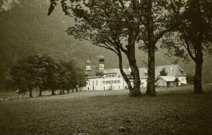 Schönau am Königssee. Sankt Bartholomäus (um 1698/1700, 1868 Weihe nach Erneuerung, 1902/1904 Renovierung) und ehemaliges Jagdschloss (1506/1522) auf der Halbinsel Hirschau am Königssee. Ansicht von der Insel