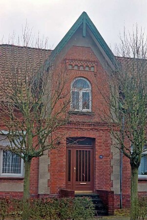 Sattenfelde: Bahnhofstraße 38: traufständiges Backsteinhaus: Straßenfront, Teilansicht: Mittelrisalit mit Dreiecksgiebel, Eingangstür, Hausnummer: davor zwei Bäume