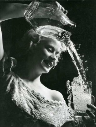 Das Modell Eva Roscher gießt Wasser aus einer Karaffe in ein Glas. Wasser läuft über. Aufnahme für einen Prospekt der Hamburger Wasserwerke aus dem Jahr 1956
