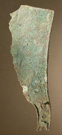 Einschneidiges breites gekrümmtes Messer. Rasiermesser? Am Griffende auf der einen Seite eine kittartige Masse, in deren Oberfläche ein längsgefaserter Stoff (Holz?) abgedrückt ist, vielleicht der Rest der Verschalung selbst (Bein oder Elfenbein?)