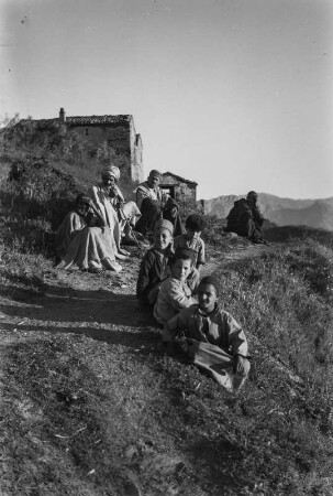Männer und Jungen der Kabylen : Eine Gruppe der Kabylen sitzt am Wegesrand vor einem Dorf.