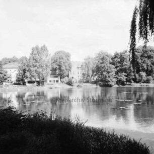 Mühlenteich: Blick von Süden Am Mühlenteich auf gegenüberliegendes Ufer: hinten links zwischen Bäumen Elektriziätswerk Reinbek-Wentorf GmbH [später: e-werk Sachsenwald]: hinten Mitte Schloss Reinbek hinter Bäumen: vorn Gräser und links Baumzweige