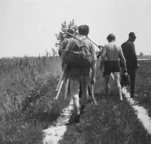 Familienbilder : Personengruppe auf einem Feldweg wohl am Ufer eines Teiches, Rückansicht