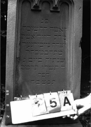 Grabstein 15 (Index: 100101732) Material: Sandstein Zustand: leicht beschädigt, Aufsatz fehlt Maße HxBxT: 163x50x38 cm Beschreibung: konische Stele, profilierter Sockel, Abdeckplatte mit Aufsatz, Schriftfeld eingetieft Symbolik: gestelztes Rundbogenfries Steinmetz: Epple: Grabstein 15A