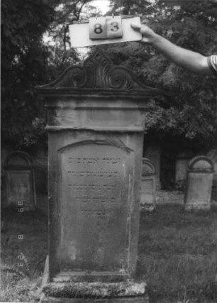 Grabstein 83 (Index: 100110797) Material: Sandstein Zustand: Beschädigung am Giebel Maße HxBxT: 151x62x34 cm Beschreibung: Stele, Sockel profiliert, Abschluß mit Voluten und Mittelakroter: Grabstein 83