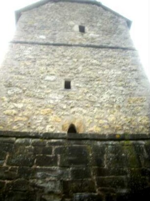 Evangelische Kirche - Kirchturm (gotisch gegründet) von Osten mit Schießscharten (Schlitzscharten) in den Geschossen sowie Werksteinen im Mauersteinverband über Kirchhofmauer