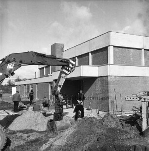 Sporteinrichtungen: Sporthalle: Barsbütteler Weg: Neubau vor Fertigstellung: Außenansicht: vorn links Bagger und Sandhügel: dahinter Arbeiter beim Verlegen der Gehwegplatten mit Schubkarre und Plattenstapel
