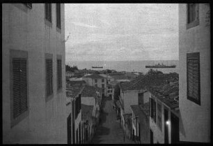 Funchal, Madeira. Blick durch eine steil zum Meer abfallende Straße mit Wohnhäusern zur Küste mit einem Hochseepassagierdampfer der Hapag auf Reede