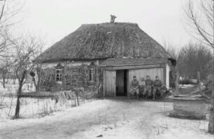 Zweiter Weltkrieg. Zur Einquartierung. Sowjetunion. Angehörige der Deutschen Wehrmacht und Einheimische, vor einer Bauernhütte sitzend