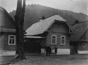 Holzhäuser : Blick auf mehrere Holzhäuser. Vor einem der Häuser steht eine Familie.