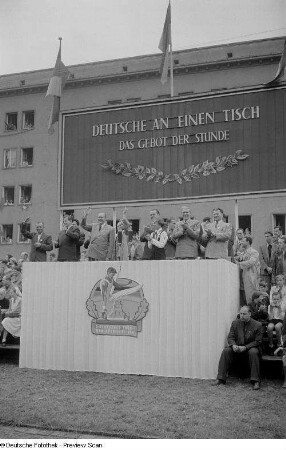 Blick auf die Tribüne mit Otto Grotewohl (3.v.l.), Erich Uhlich (3.v.r.), Max Reimann (2.v.r.) und Paul Fröhlich (rechts) auf der Straße der III. Weltfestspiele (heutige Jahnallee)
