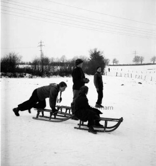 Kinder mit Schlitten: dahinter Knicklandschaft mit Strommasten: Winter