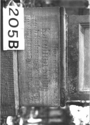 Grabstein 205 (Index: 99899100) Material: Sandstein Zustand: gut erhalten, am Sockel beginnende Verwitterung Maße HxBxT: 172x48x23 cm Beschreibung: aufgesockelte Stele, überkragender Giebelaufsatz mit Akroterien, im Giebelfeld geometrisches Ornament, Giebelaufsatz?, Schriftfeld eingetieft: Grabstein 205B